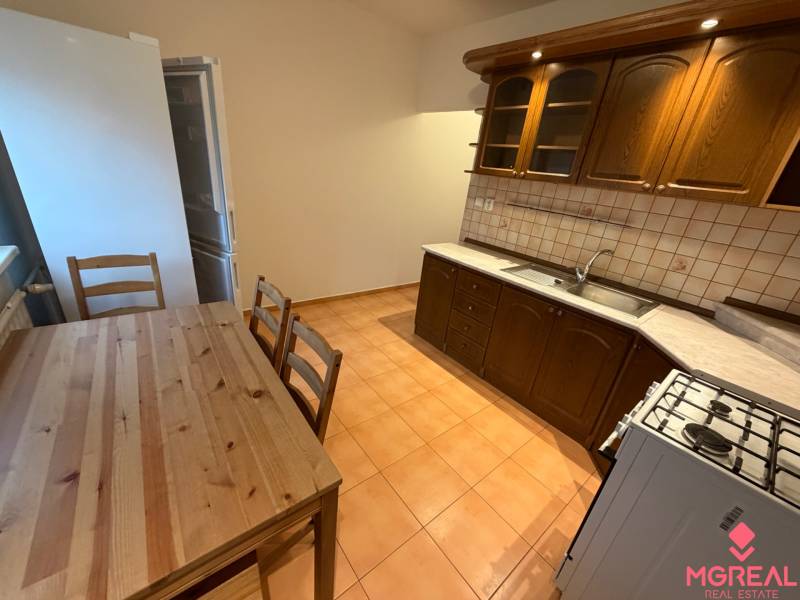 A kitchen in a 3-room apartment with a table and wooden cabinets, flooring with a wood decor.