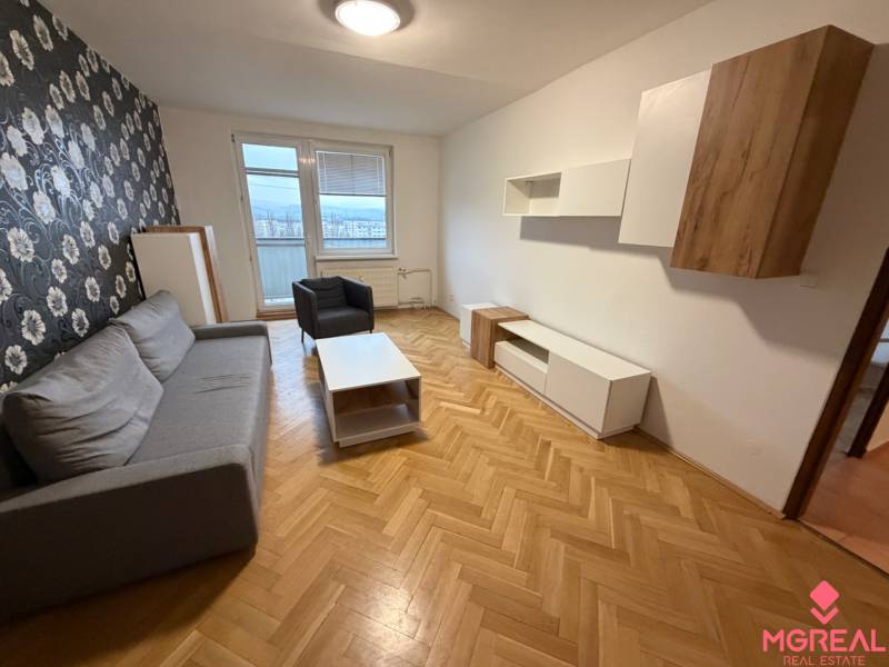 A living room in a 3-room apartment with a gray sofa and floral wallpaper on the wall.