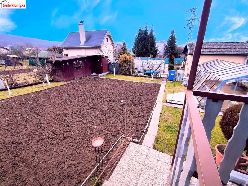 A garden with raised beds and trees around a cottage in Partizánske.