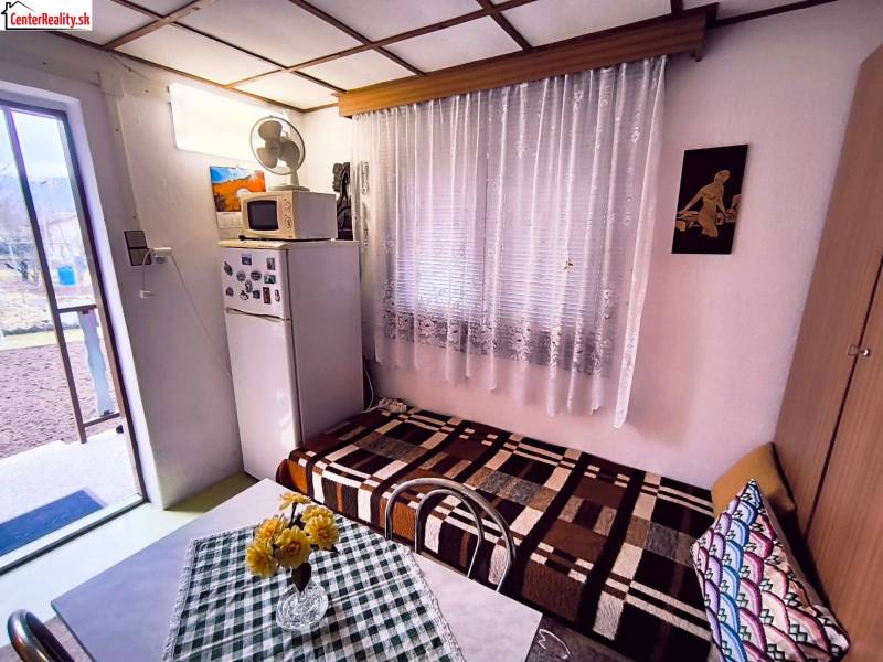 The interior of the cottage with a refrigerator, sofa, table, and a view of the garden.