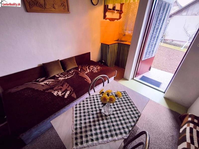 The interior of a cottage with a sofa, dining table, and open doors to the garden.