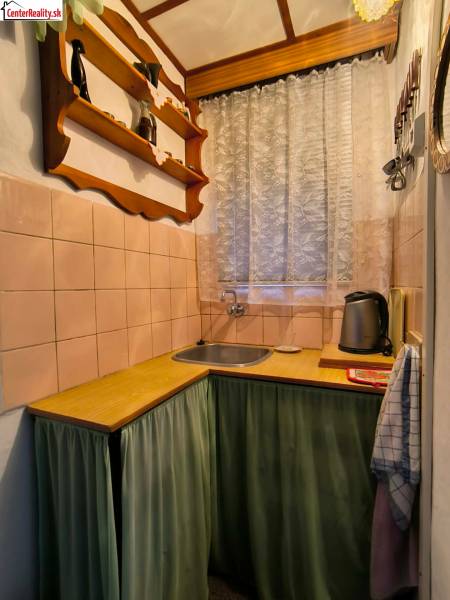 A kitchen in a cottage with wooden decor, a shelf, and a curtain by the window.