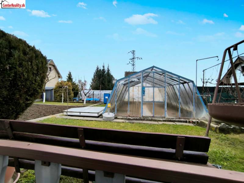 A garden in Partizánske with a greenhouse, grass, and a small flowerbed.
