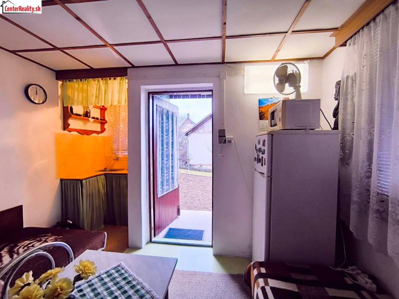 The interior of a cabin with a kitchenette, a sofa, and open doors to the garden.