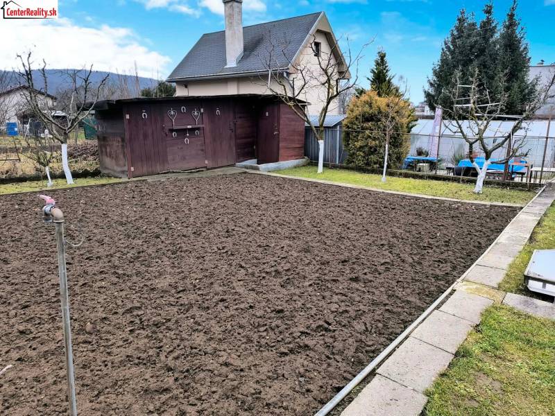 A garden with a cottage in Partizánske, a prepared flowerbed, surrounding greenery, and a wooden house.