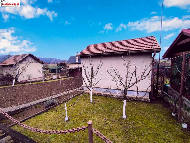 A garden with a cottage in Partizánske, fruit trees and cultivated land, clear sky.