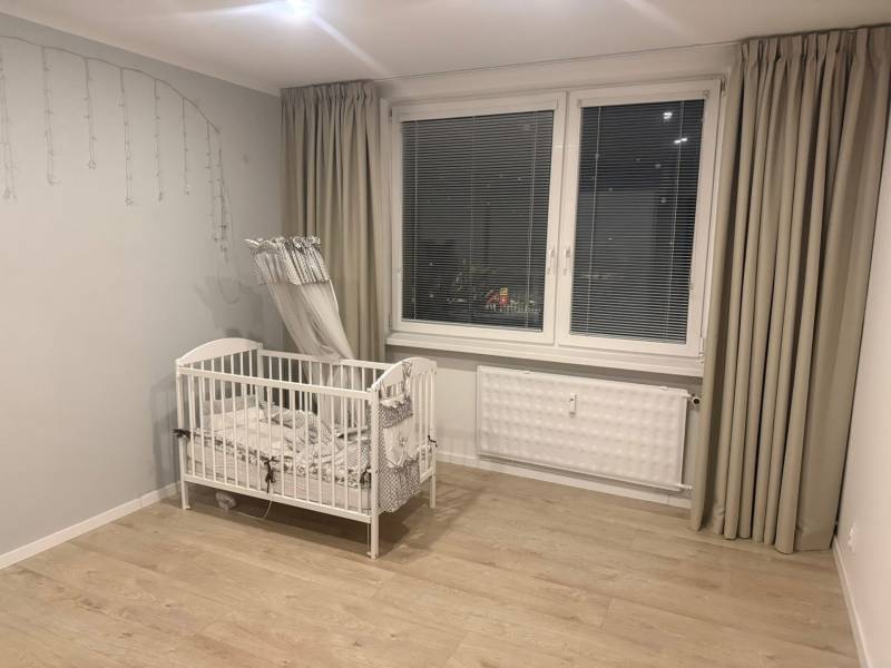 A crib in a 3-room apartment with a wood-patterned floor and gray curtains.