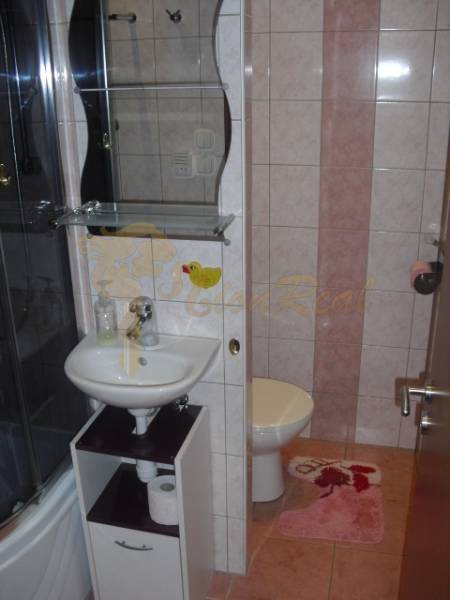 A bathroom in a studio apartment with a sink, shower, and light tiles.