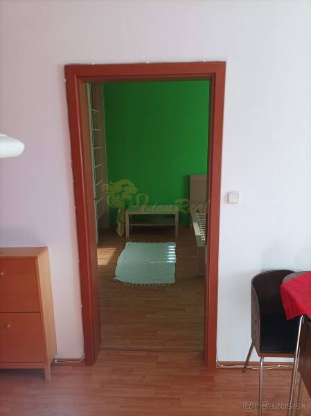 A room with a bed, green wall, wooden decor flooring, furniture in a studio apartment.