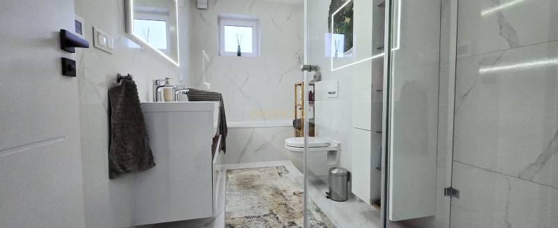 A bathroom in a family house with marble tiles, a mirror, and a shower enclosure.