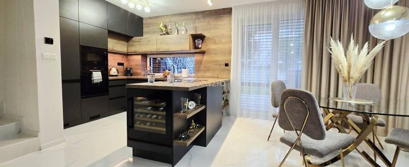 A kitchen in a family house with an island, black cabinets, and a wine cooler.