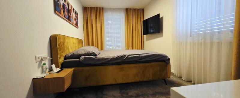 Bedroom in a family house with a bed, nightstand, TV, and curtains.