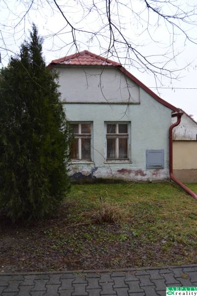 A family house in Abrahám with colorful plaster and two windows, surrounded by greenery.