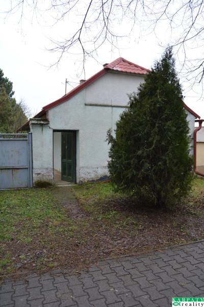 A family house in Abrahám with a red roof, a green gate, and a tree in the yard.