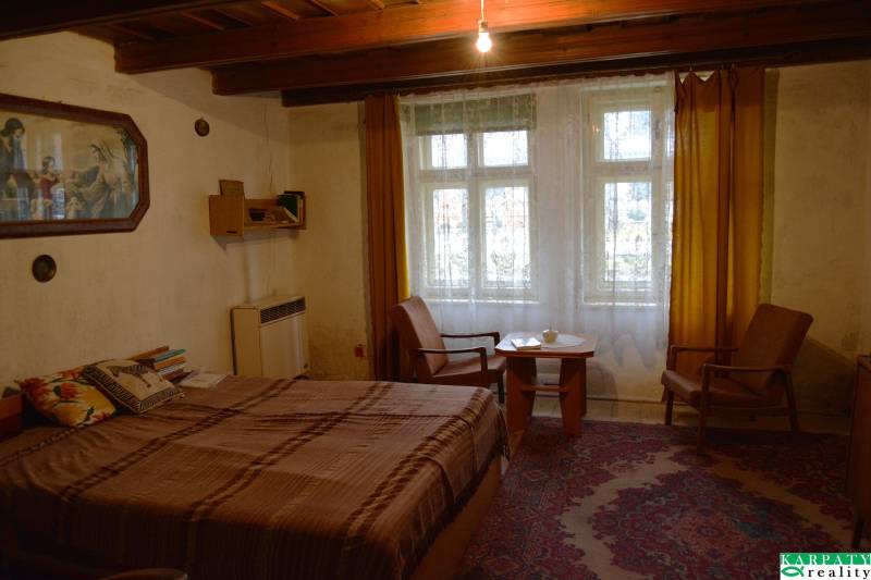 A room in a family house with a bed, chairs, yellow curtains, and a carpet.