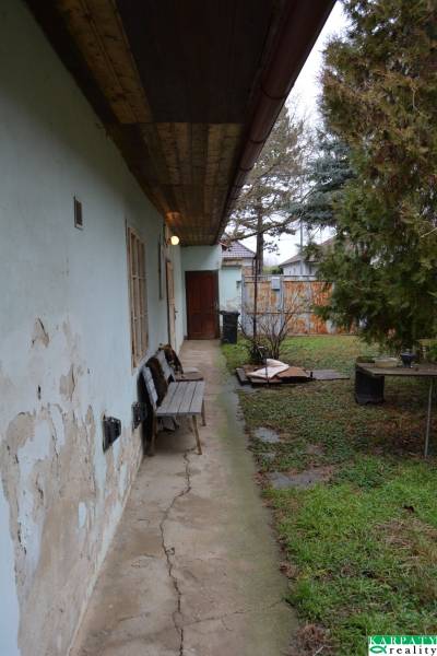 A family house in Abrahám with a bench on a damaged concrete walkway and an overgrown garden.