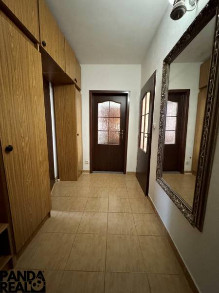 A hallway in a 3-room apartment with a tiled floor, a mirror, and wood decor cabinets.