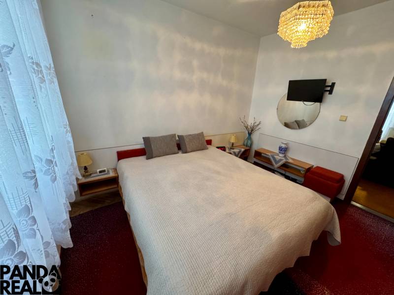 A bedroom in a 3-room apartment with a bed, a chandelier, and a TV on the wall.