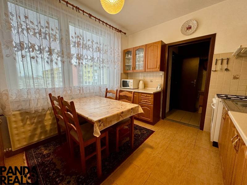 A kitchen in a 3-room apartment with a wooden decor, dining table, and curtains.