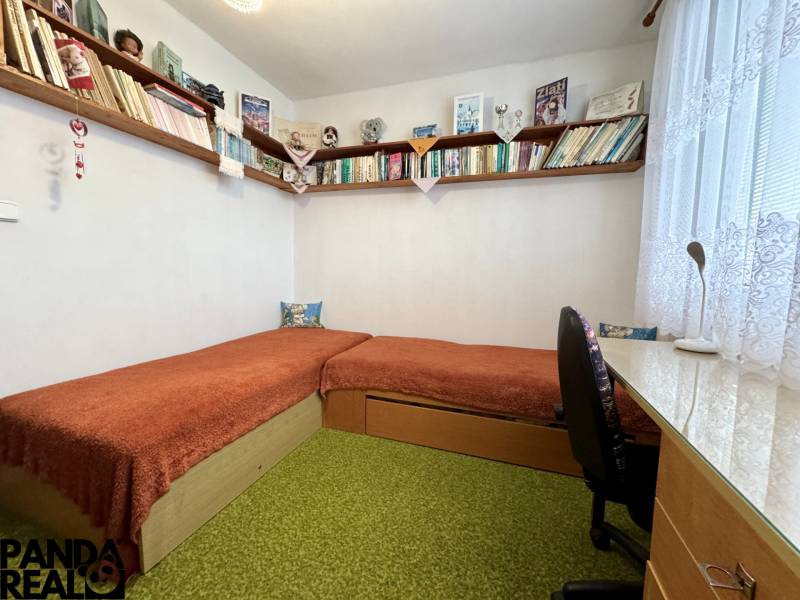 A room in a 3-room apartment with shelves full of books and a simple desk.