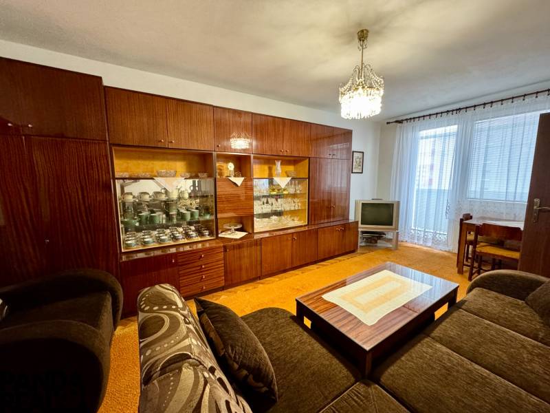 Living room with a rustic wall unit and TV in a three-room apartment.