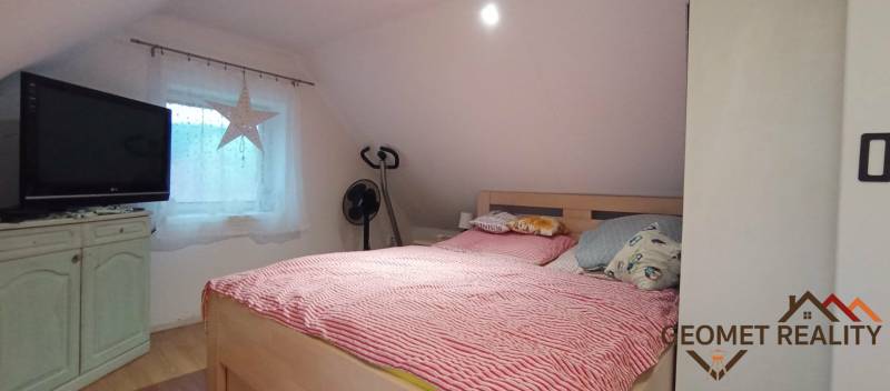 An attic bedroom in a family house with a bed, television, and a wooden decor floor.
