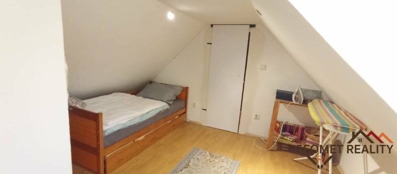 Attic room with a sloped wall, bed, and wooden decor flooring in a family house.