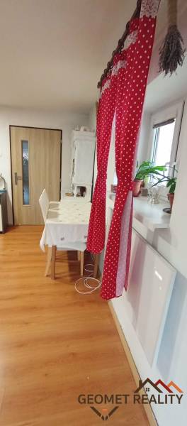 A dining room in a family house with a red curtain, a table, and a wooden-patterned floor.