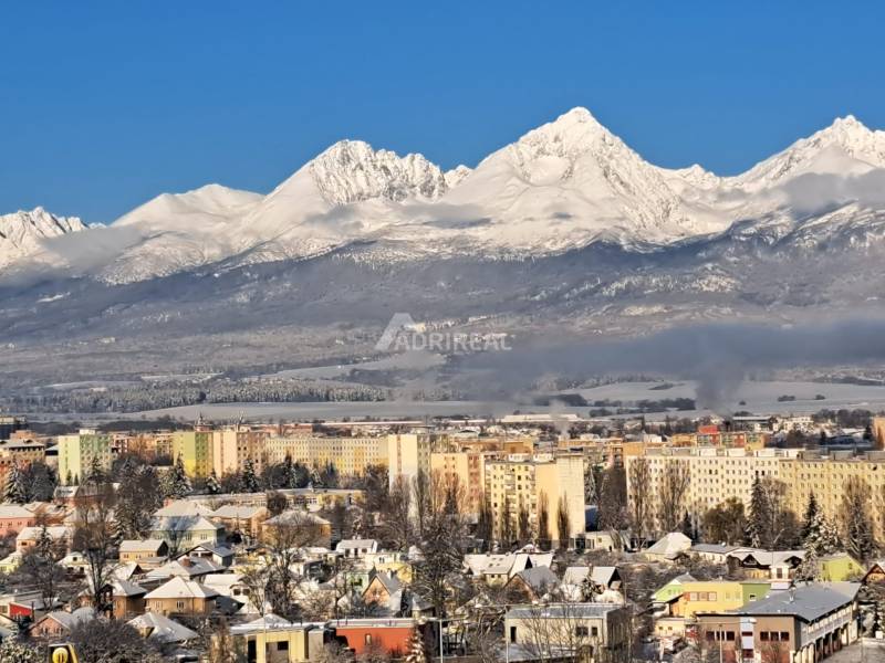 Snow-covered mountains with a view of part of the city of Poprad and multi-story buildings.