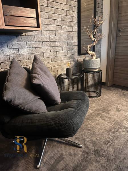 A stylish armchair in a 2-room apartment, gray bricks, decorative tree, dark textiles.