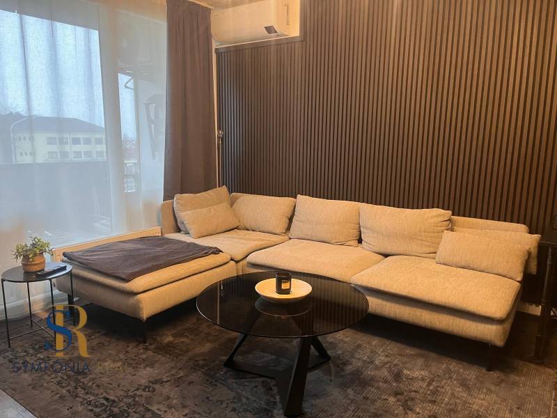 A light sofa in a 2-room apartment with wooden decor on the wall and a table.