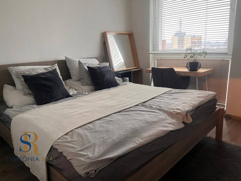 Bedroom in a 2-room apartment with a bed, a desk, and a wooden decor floor.