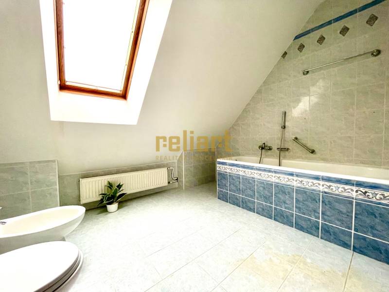 Attic bathroom with a corner bathtub and a skylight in a family house.