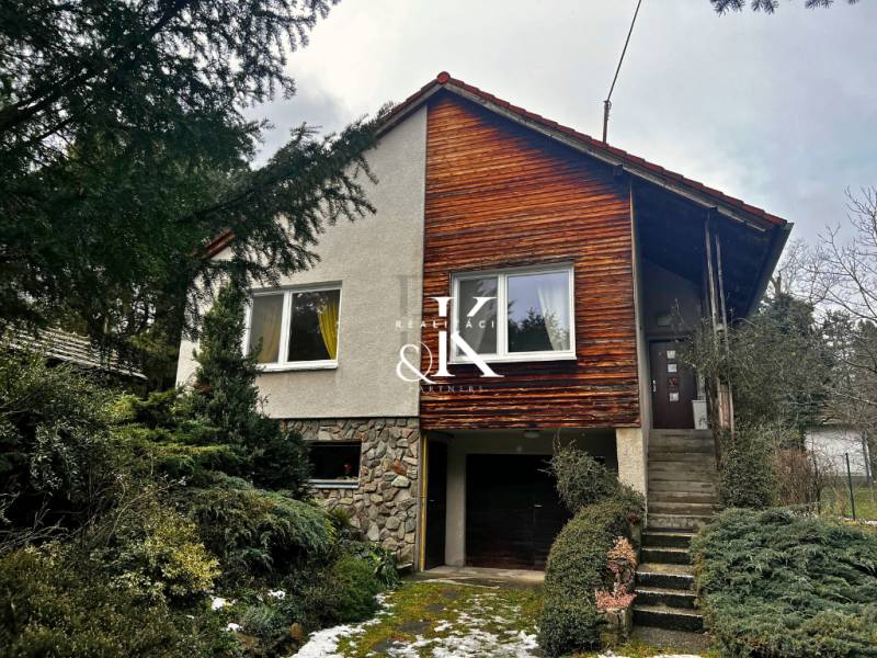 A cottage in Modra with wooden cladding and a garage, surrounded by greenery.