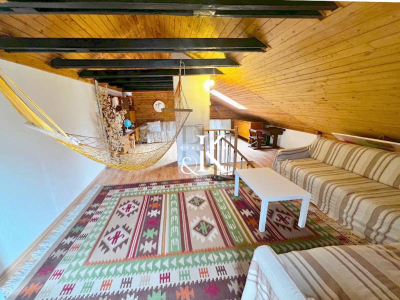 The attic of a cottage with a sofa, a hammock, and a wooden decor floor.