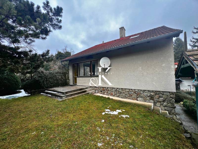 A cottage near Modra with a grassy plot, stone steps, and coniferous trees.