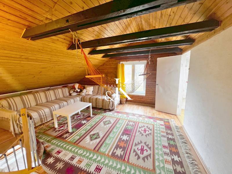 The attic of the cottage with a wooden ceiling, a striped sofa, and a hanging swing chair.