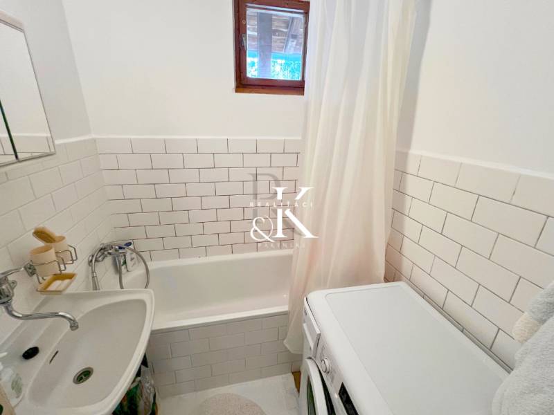 A bathroom in a cottage with a bathtub, a washing machine, and white tiles.