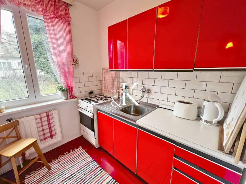 A small kitchen in a cottage with red cabinets, tiles, and appliances.