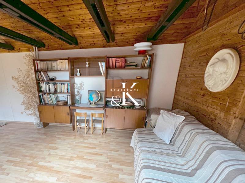The interior of a cabin with wooden beams, furniture, and a wooden-patterned floor.