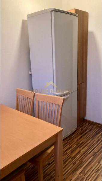 Kitchen in a 3-room apartment with a refrigerator, wooden table and chairs, floor with wooden decor.