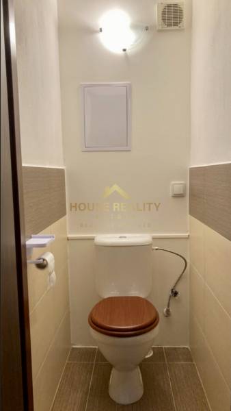 A toilet with a white wall, brown tiles, and a white toilet, 3-room apartment.