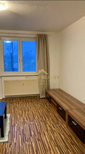 Living room in a three-room apartment with a wooden decor floor and a view through a large window.