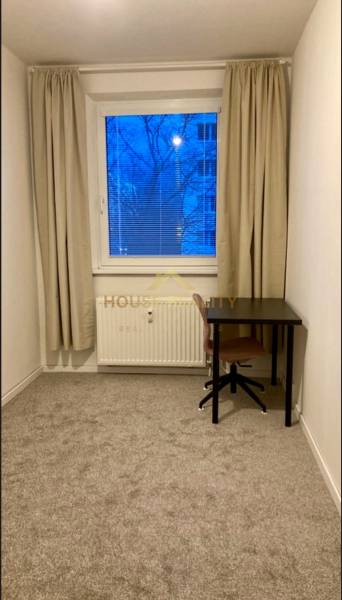 A room in a 3-room apartment with a desk and carpeted floor.