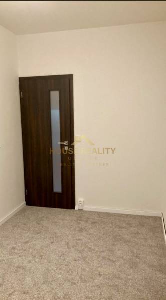 A room in a 3-room apartment with carpet flooring and dark doors.