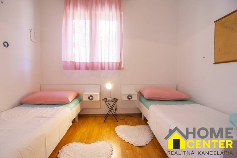 A bright bedroom with two beds, pink curtains, and a wood-patterned floor.