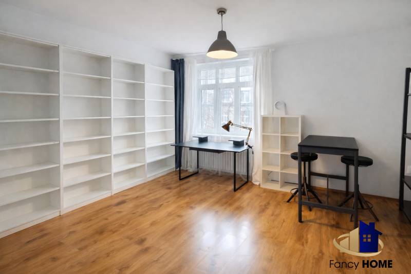 A spacious room with shelves, a table, and a wooden-patterned floor in a two-room apartment.