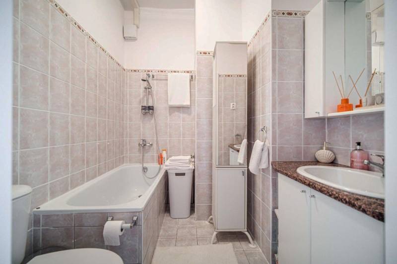 Bathroom in a studio apartment with a bathtub, sink, and ceramic tiles in neutral shades.
