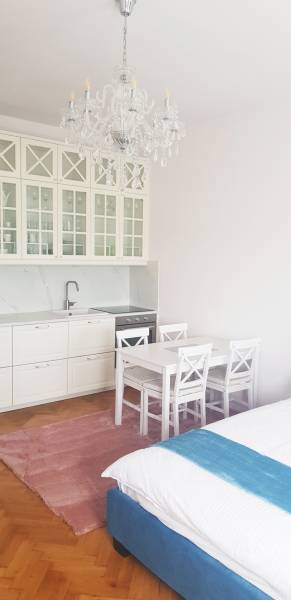 A kitchenette with white furniture, a table, and a crystal chandelier in a studio apartment.