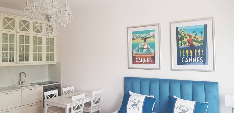 Interior of a 1-room apartment with a kitchen, chandelier, and paintings above a blue bed.